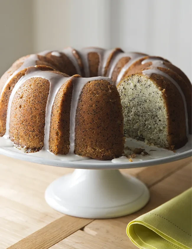 Ina Garten lemon poppy seed cake on a plate, showing the golden Bundt shape with white lemon glaze drizzled over the top and poppy seeds visible throughout