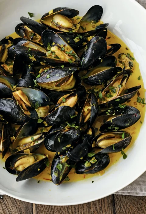 A bowl of steamed mussels in saffron cream broth with fresh herbs and crusty bread, Ina Garten mussels with saffron cream