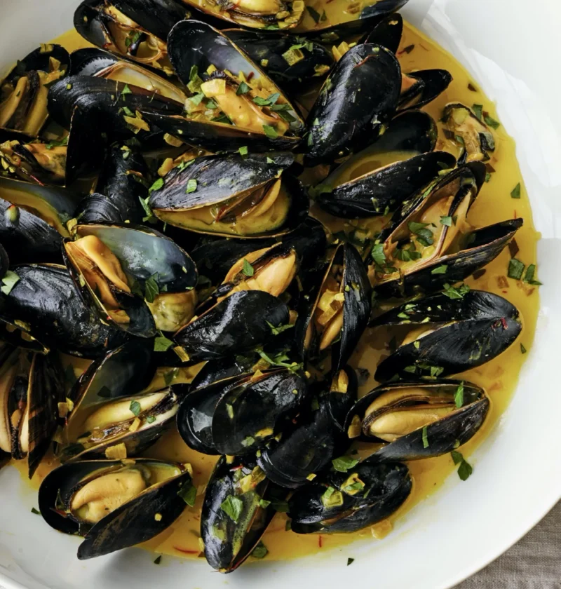 A bowl of steamed mussels in saffron cream broth with fresh herbs and crusty bread, Ina Garten mussels with saffron cream