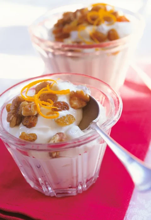A bowl of Ina Garten orange yogurt topped with walnuts, raisins, and fresh orange zest