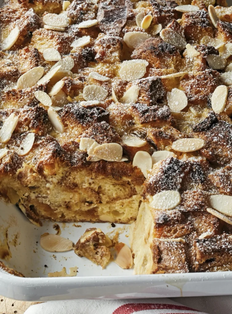 Ina Garten panettone bread pudding in a baking dish topped with sliced almonds and dusted with confectioners sugar