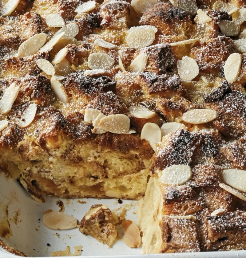Ina Garten panettone bread pudding in a baking dish topped with sliced almonds and dusted with confectioners sugar