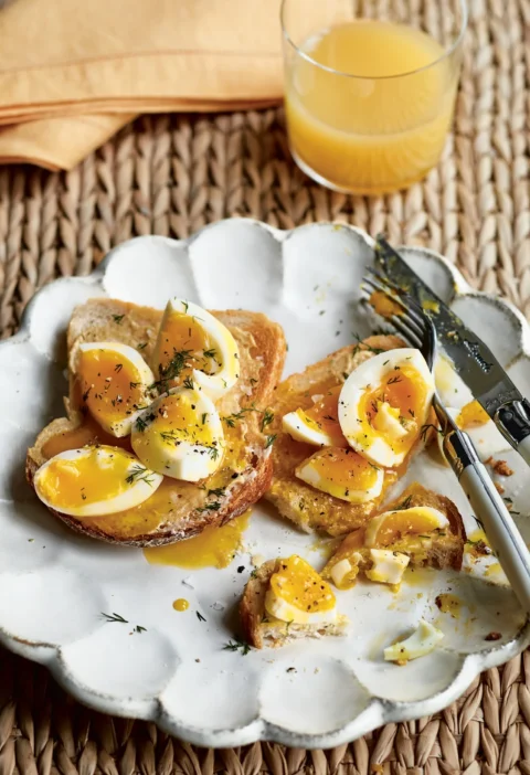 Ina Garten smashed eggs on toast with runny yolk, fresh dill and cracked pepper on a white scalloped plate