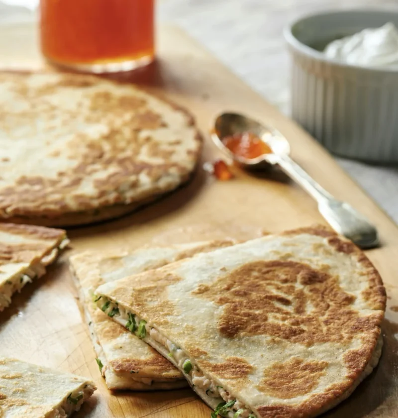 Ina Garten smoked salmon quesadillas cut into wedges on a wooden board, showing the creamy salmon and dill filling, with sour cream and salmon roe alongside
