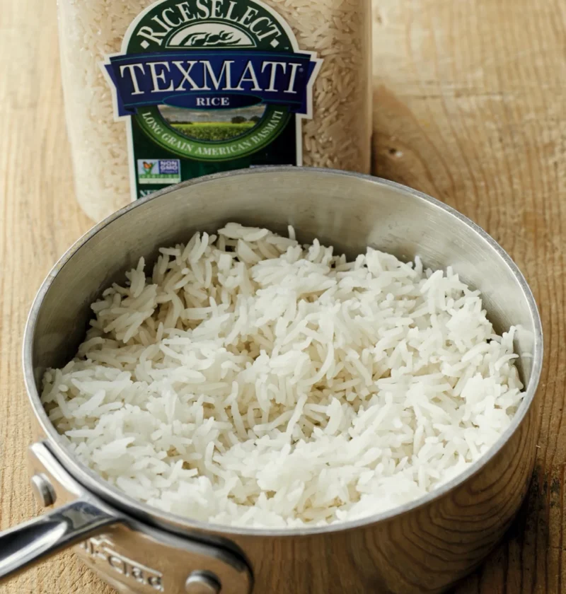 Ina Garten steamed basmati rice fluffed in a stainless steel saucepan with a jar of RiceSelect Texmati rice on a wood table