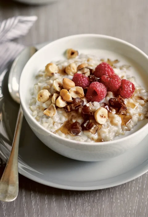A warm whole-grain breakfast bowl with chewy pearled barley, creamy oats, dried dates, fresh raspberries, and toasted hazelnuts drizzled with maple syrup