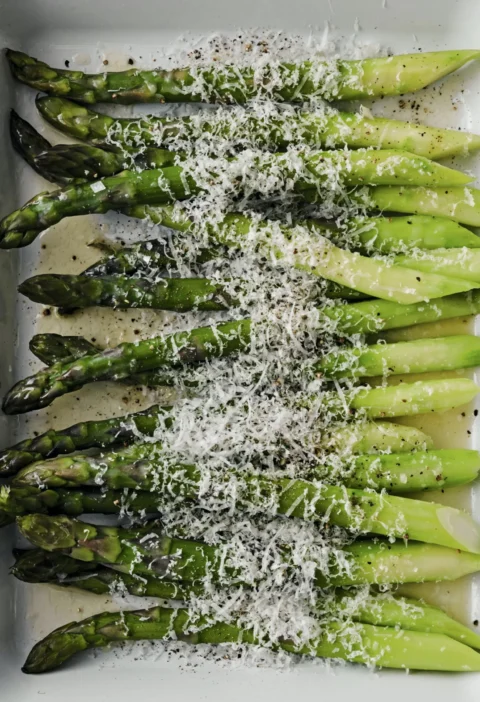 Thick asparagus spears roasted with melted Pecorino and Parmesan cheese in a white baking dish, Ina Garten asparagus cacio e pepe