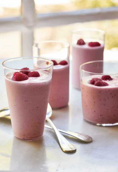 Two tall glasses of Ina Garten berries and jam milkshakes topped with fresh raspberries on a table