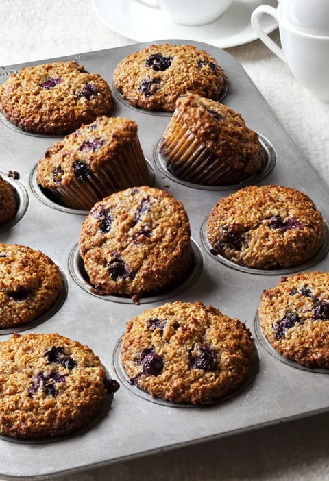 A batch of freshly baked Ina Garten blueberry bran muffins in paper liners with golden brown tops