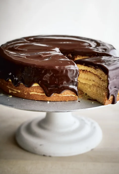 Ina Garten boston cream pie with chocolate glaze dripping down the sides of a four-layer vanilla cake