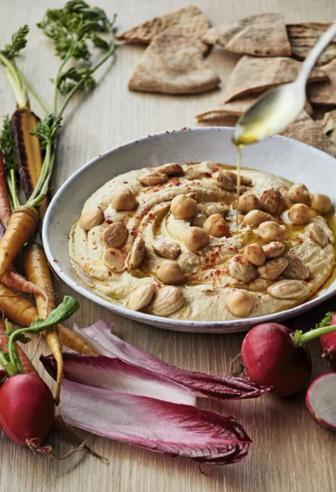 A plate of creamy Ina Garten hummus topped with whole chickpeas, chopped Marcona almonds, and smoked paprika