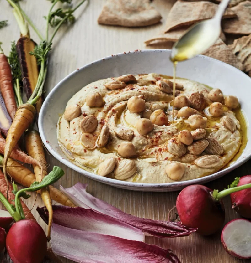 A plate of creamy Ina Garten hummus topped with whole chickpeas, chopped Marcona almonds, and smoked paprika