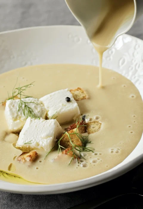 A bowl of creamy potato fennel soup topped with goat cheese crumbles, bacon, and fresh fennel fronds, showing the velvety puréed texture of ina garten creamy potato fennel soup