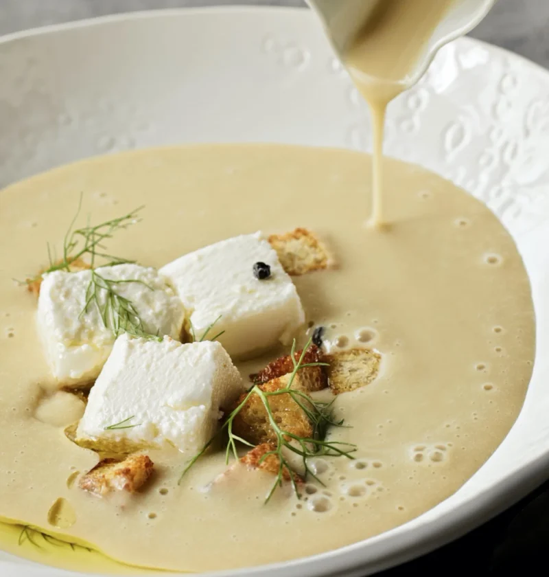 A bowl of creamy potato fennel soup topped with goat cheese crumbles, bacon, and fresh fennel fronds, showing the velvety puréed texture of ina garten creamy potato fennel soup