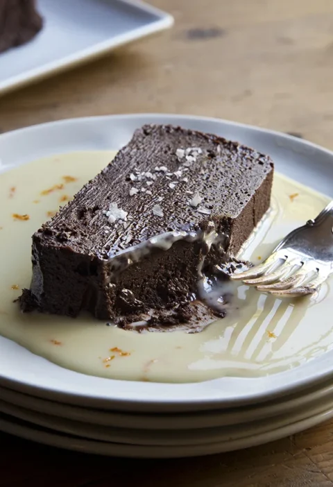 Sliced dark chocolate terrine with orange sauce drizzled on a dessert plate, topped with orange zest and fleur de sel