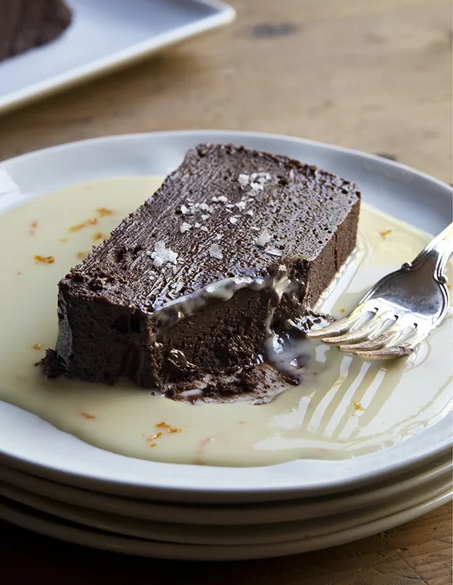 Sliced dark chocolate terrine with orange sauce drizzled on a dessert plate, topped with orange zest and fleur de sel