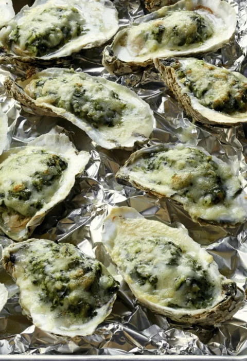 Easy oysters Rockefeller topped with creamed spinach and melted Parmesan and Gruyère cheese on a foil-lined baking sheet