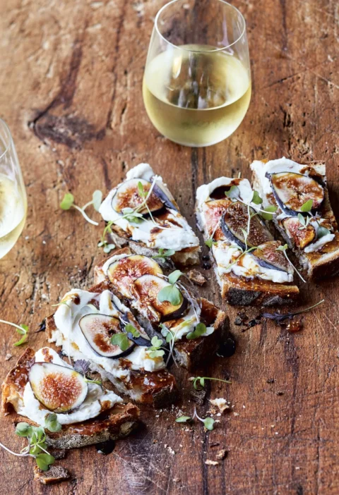 Ina Garten fig and cheese toasts topped with fresh fig slices, microgreens, and balsamic drizzle on a serving board