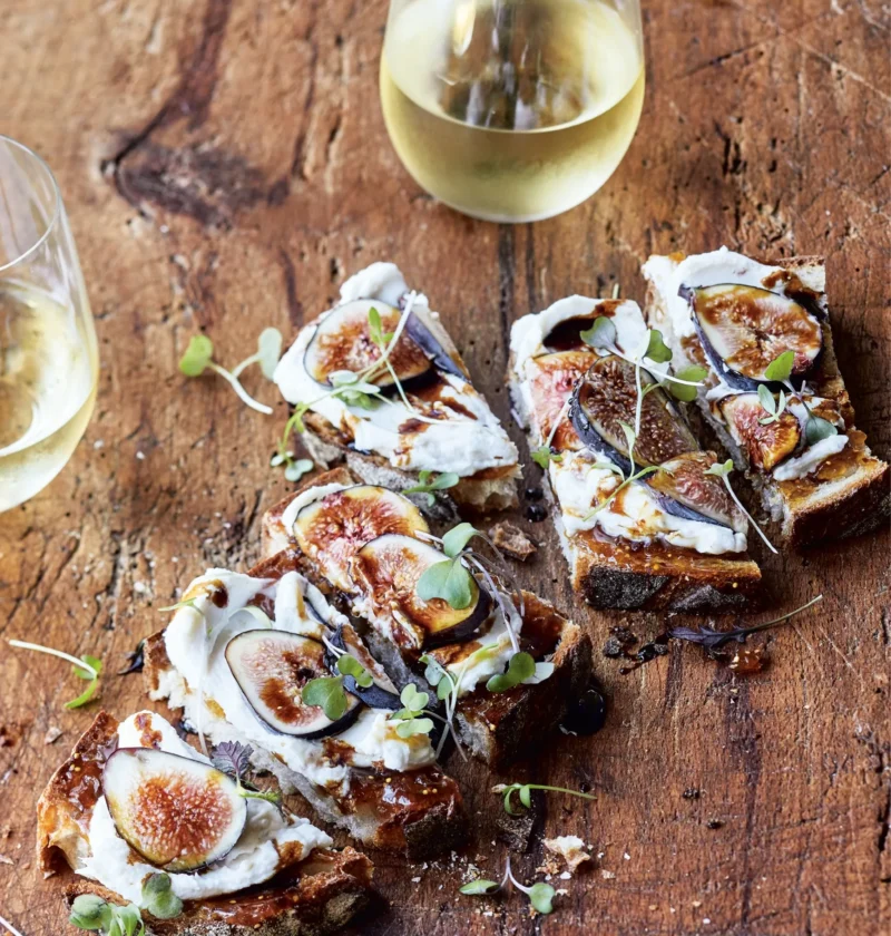 Ina Garten fig and cheese toasts topped with fresh fig slices, microgreens, and balsamic drizzle on a serving board