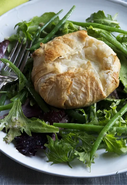 A plate of French green bean salad topped with a golden phyllo-wrapped warm goat cheese package, dressed in dill vinaigrette