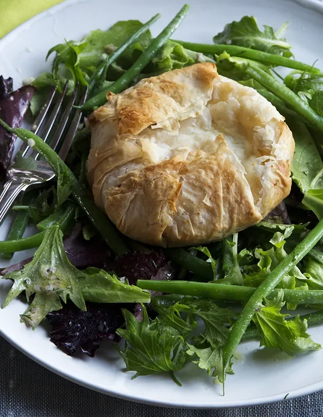 A plate of French green bean salad topped with a golden phyllo-wrapped warm goat cheese package, dressed in dill vinaigrette