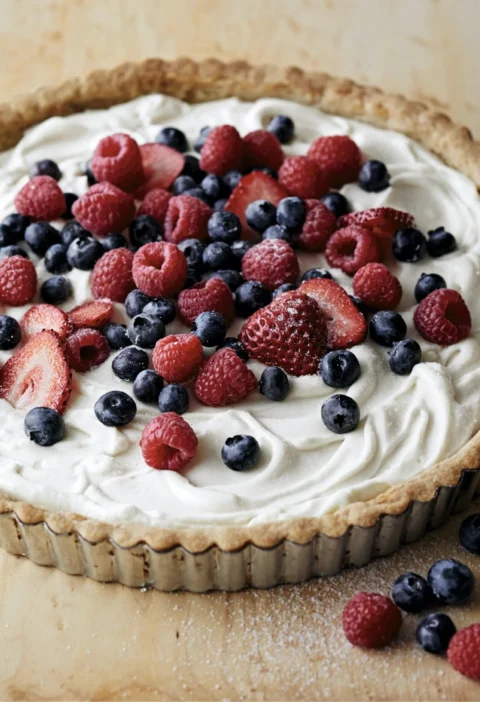 A fresh berry and mascarpone tart topped with sliced strawberries, raspberries, and blueberries on a golden shortbread crust