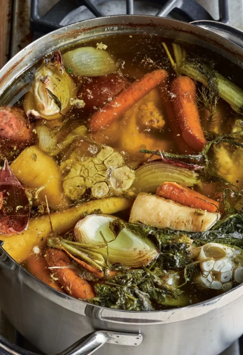 A pot of golden homemade chicken stock made with Ina Garten recipe simmering with fresh herbs and vegetables