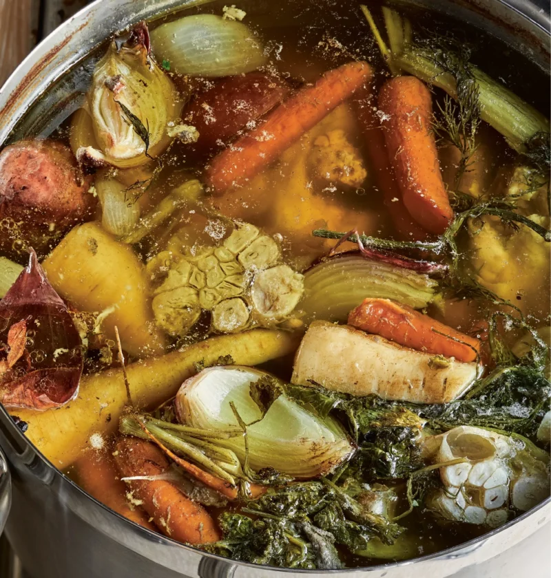 A pot of golden homemade chicken stock made with Ina Garten recipe simmering with fresh herbs and vegetables