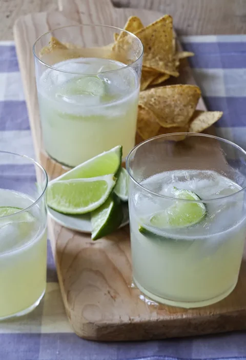 Two jalapeño margaritas served over ice in glasses with lime wedges, showing the pale golden tequila infused with jalapeño pepper