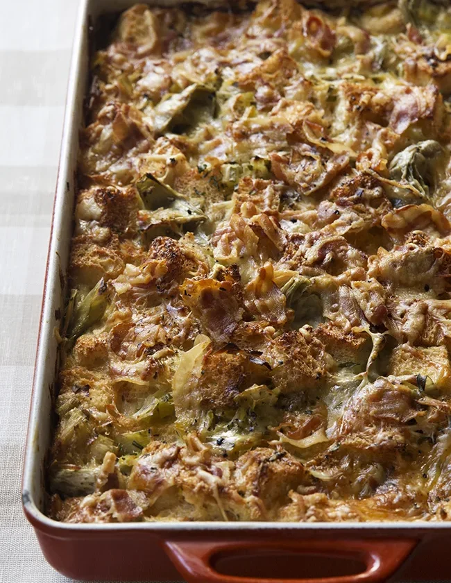 Ina Garten leek and artichoke bread pudding in a baking dish with golden cheese on top