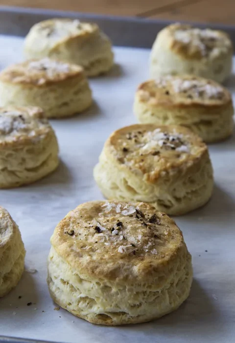 Golden baked make-ahead salt and pepper biscuits topped with flaky Maldon sea salt and cracked black pepper on a sheet pan