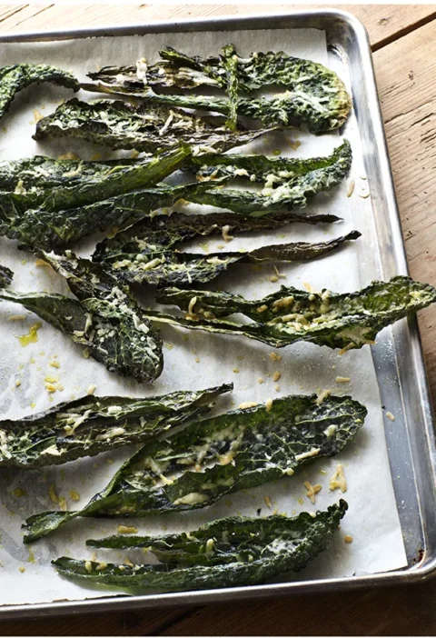 Crispy parmesan kale chips arranged on a baking sheet, showing golden-brown roasted kale leaves topped with melted Parmesan cheese