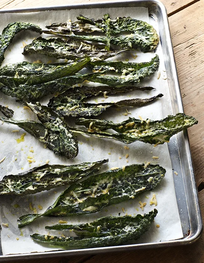Crispy parmesan kale chips arranged on a baking sheet, showing golden-brown roasted kale leaves topped with melted Parmesan cheese