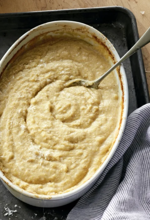 Creamy ina garten parmesan polenta baked in an oval dish topped with grated Parmesan cheese