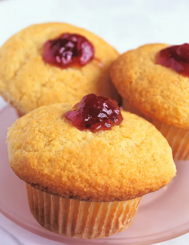 Ina Garten raspberry corn muffins with golden crisp tops and raspberry preserves piped into the center