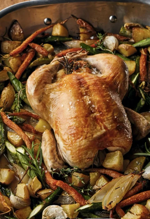 Roast chicken with spring vegetables including carrots, potatoes, and asparagus in a roasting pan, an Ina Garten roast chicken recipe