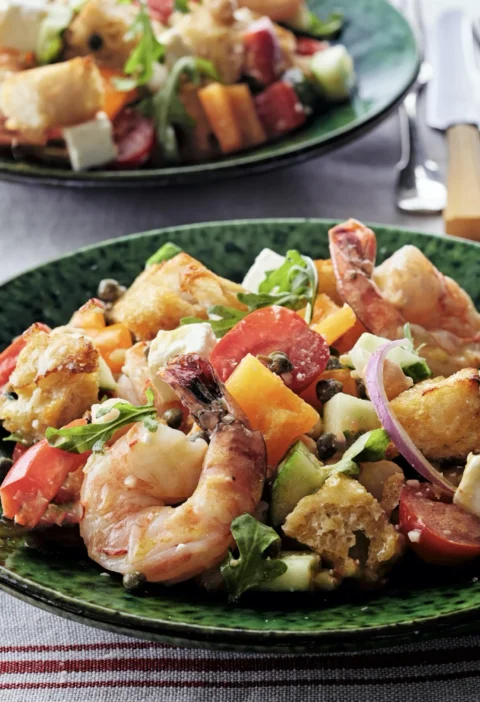 A bowl of roasted shrimp panzanella with golden croutons, cherry tomatoes, arugula, and feta in Dijon vinaigrette