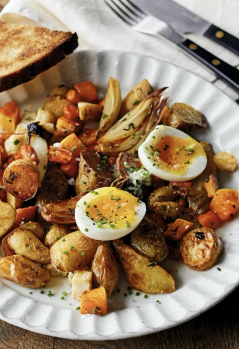 Roasted butternut squash, fingerling potatoes, celery root, and carrots on a sheet pan topped with jammy soft-boiled eggs and fresh herbs