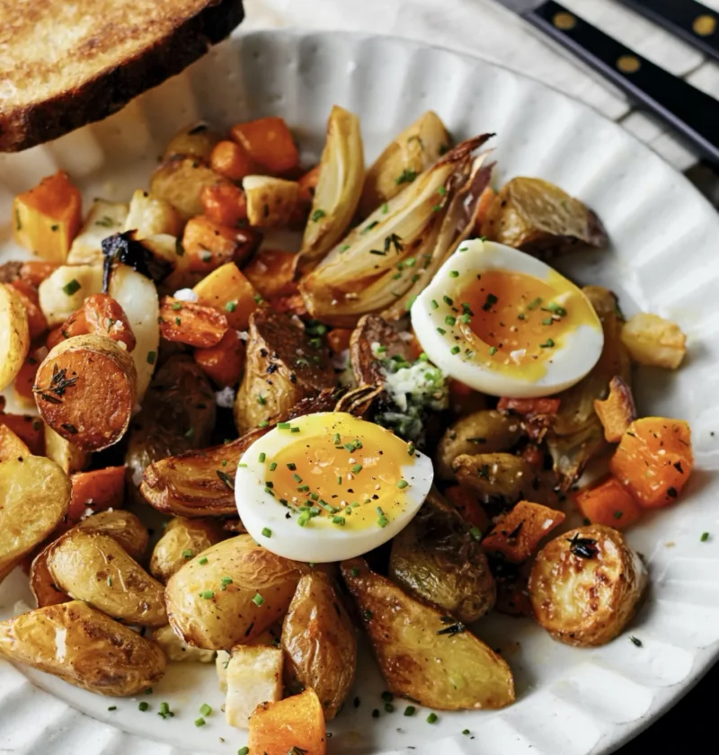 Roasted butternut squash, fingerling potatoes, celery root, and carrots on a sheet pan topped with jammy soft-boiled eggs and fresh herbs