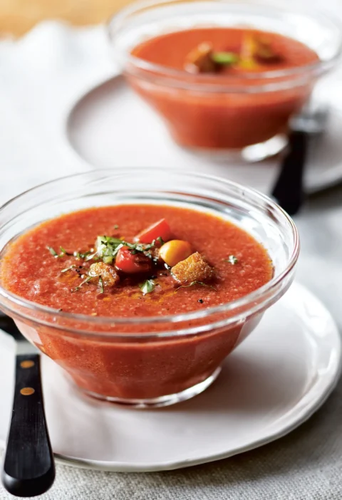 A bowl of creamy ina garten salmorejo topped with crispy croutons, halved cherry tomatoes, and fresh basil