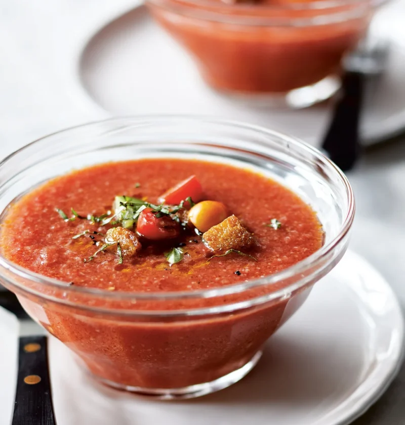 A bowl of creamy ina garten salmorejo topped with crispy croutons, halved cherry tomatoes, and fresh basil