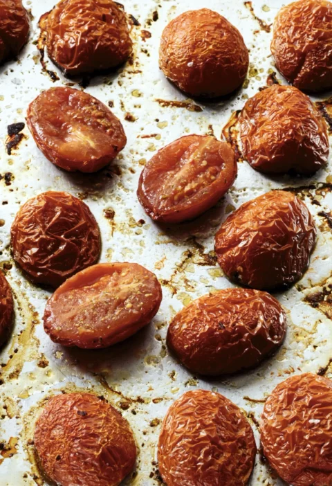 Slow-roasted plum tomatoes with fennel pollen on a sheet pan, caramelized and golden brown around the edges