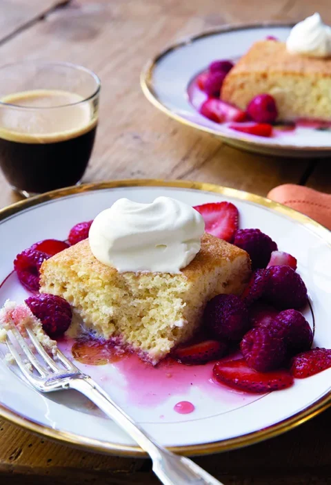 Ina Garten tres leches cake with berries on a dessert plate, dusted with confectioners sugar and topped with fresh raspberries and strawberries