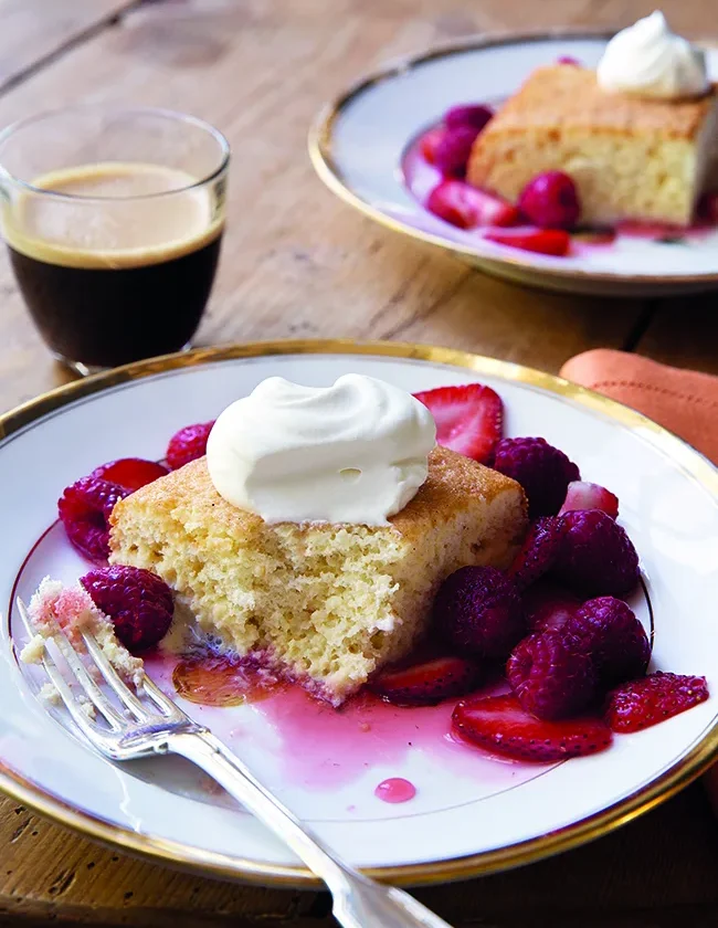Ina Garten tres leches cake with berries on a dessert plate, dusted with confectioners sugar and topped with fresh raspberries and strawberries