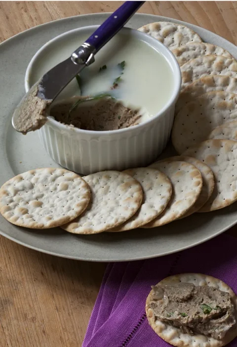 Truffled chicken liver mousse in a ramekin topped with duck fat and fresh parsley sprigs served with crackers
