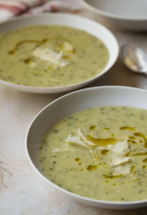 A bowl of creamy Ina Garten zucchini basil soup topped with shaved Parmesan and a drizzle of olive oil
