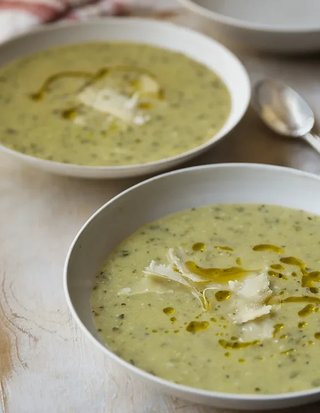 A bowl of creamy Ina Garten zucchini basil soup topped with shaved Parmesan and a drizzle of olive oil