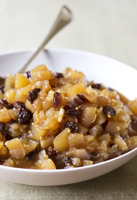 Ina Garten apple chutney with diced apples, raisins and mustard seeds in a white bowl with a spoon