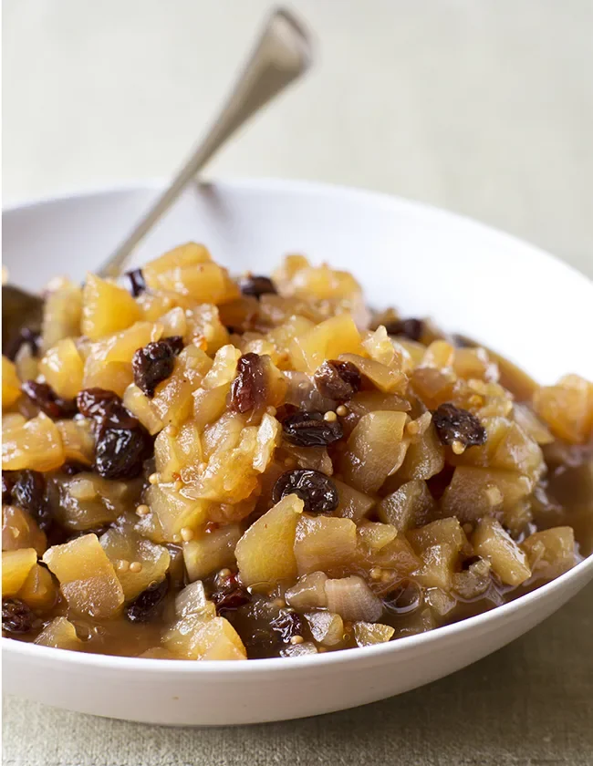 Ina Garten apple chutney with diced apples, raisins and mustard seeds in a white bowl with a spoon
