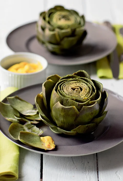 Ina Garten artichokes with lemon-tarragon aioli, whole cooked artichokes on gray plates with a small bowl of aioli